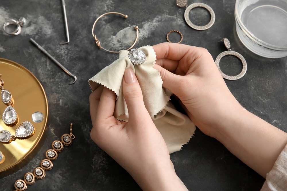 Woman Polishing Beautiful Ring With Napkin On Grunge Background Closeup