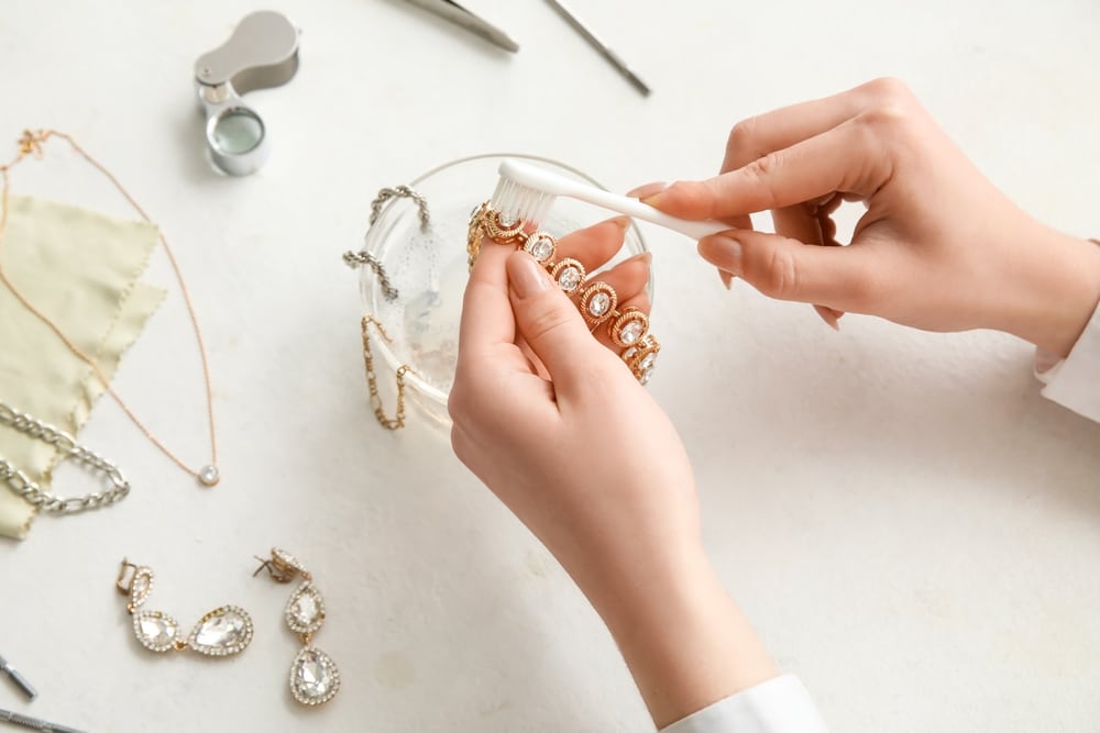 Woman Cleaning Beautiful Bracelet With Toothbrush On Light Background Closeup