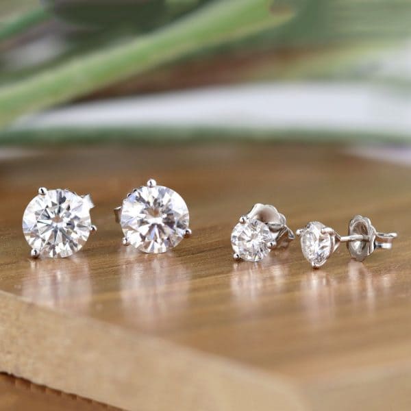 two pairs of Diamond stud earrings on a wooden platform