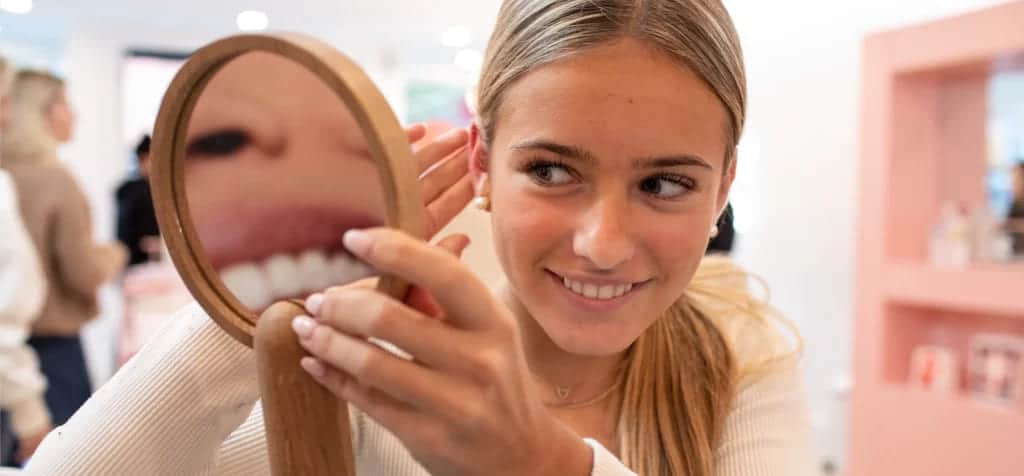 a lady with a smiling face checking her earrings in a mirror