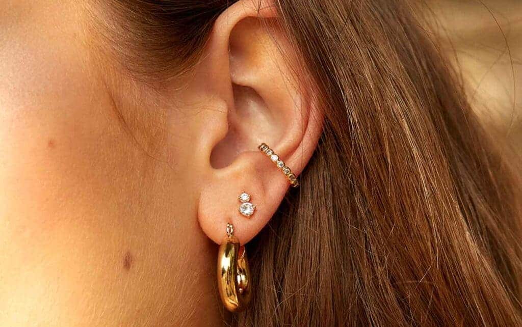 an ear of a lady golden hoop earrings and ear cuffs