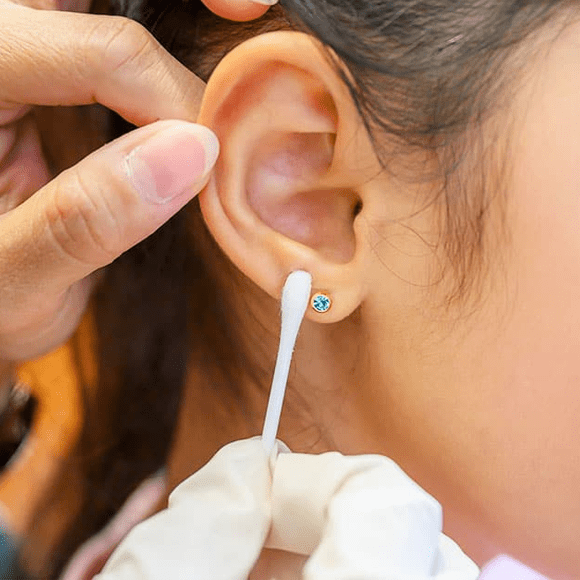 a lady cleaning ear piercing with a cotton bud