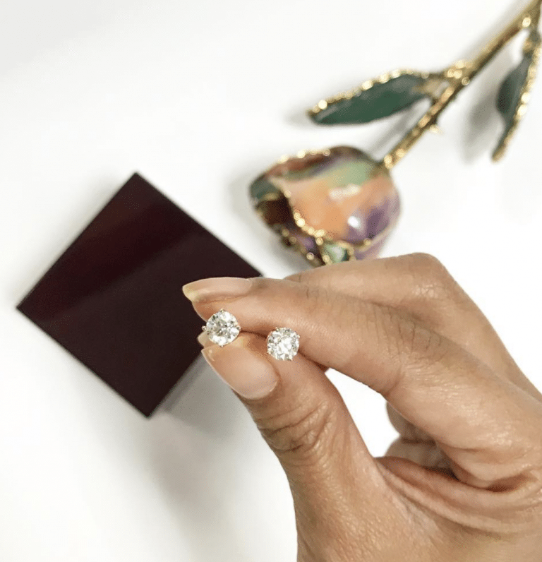 fake diamonds earrings pair held in the fingers with a decorative flower in the background