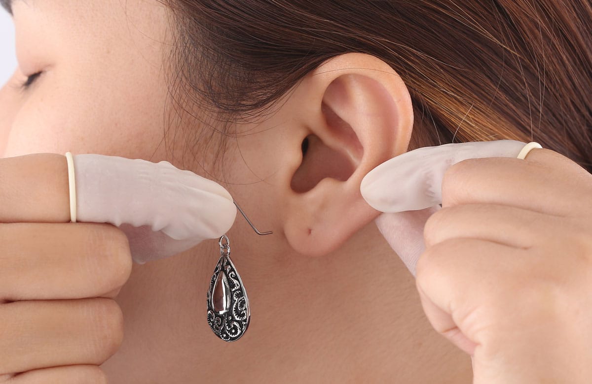 a lady holding her ear with one hand and putting earring in the ear