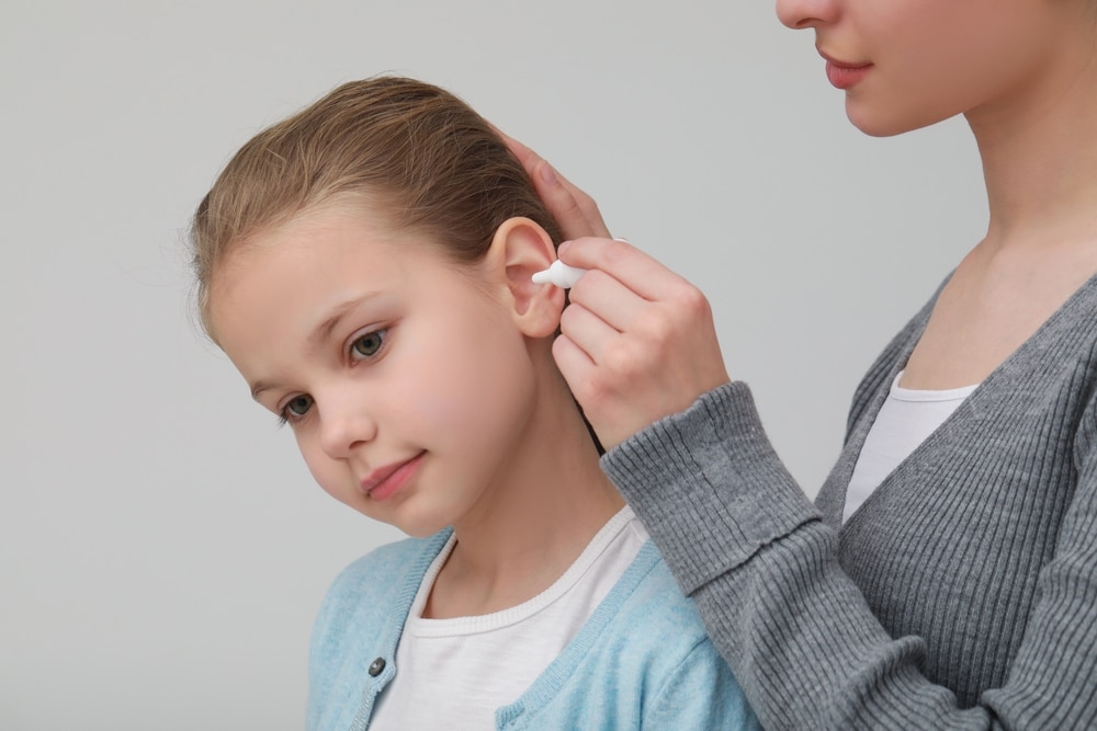 Mother Dripping Medication Into Daughter's Ear On Light Grey Background